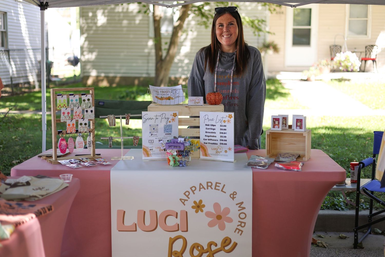 A small business vendor stands behind their decorated pink booth at an outdoor market.