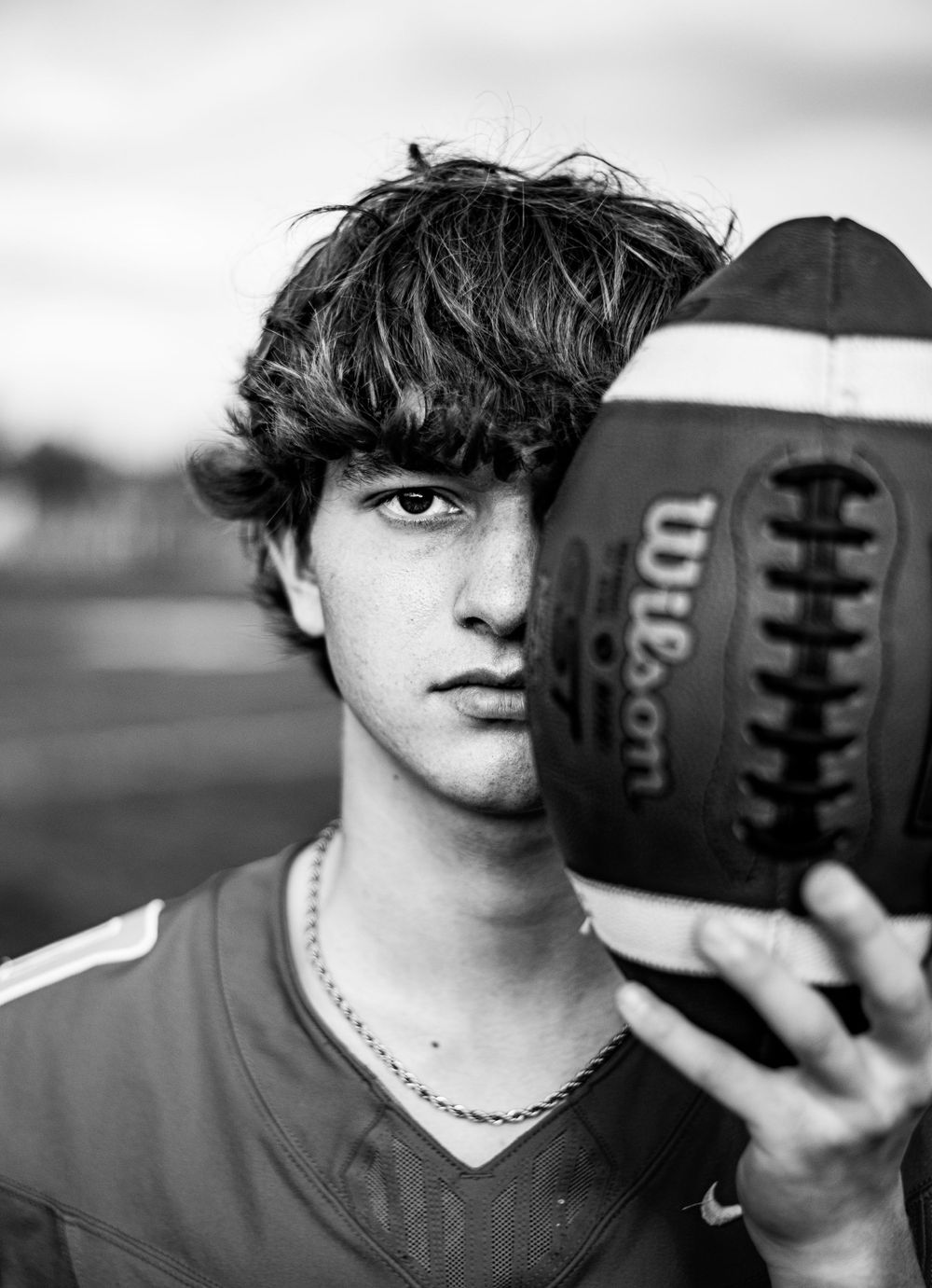 Black and white portrait of athlete holding football against cloudy sky.