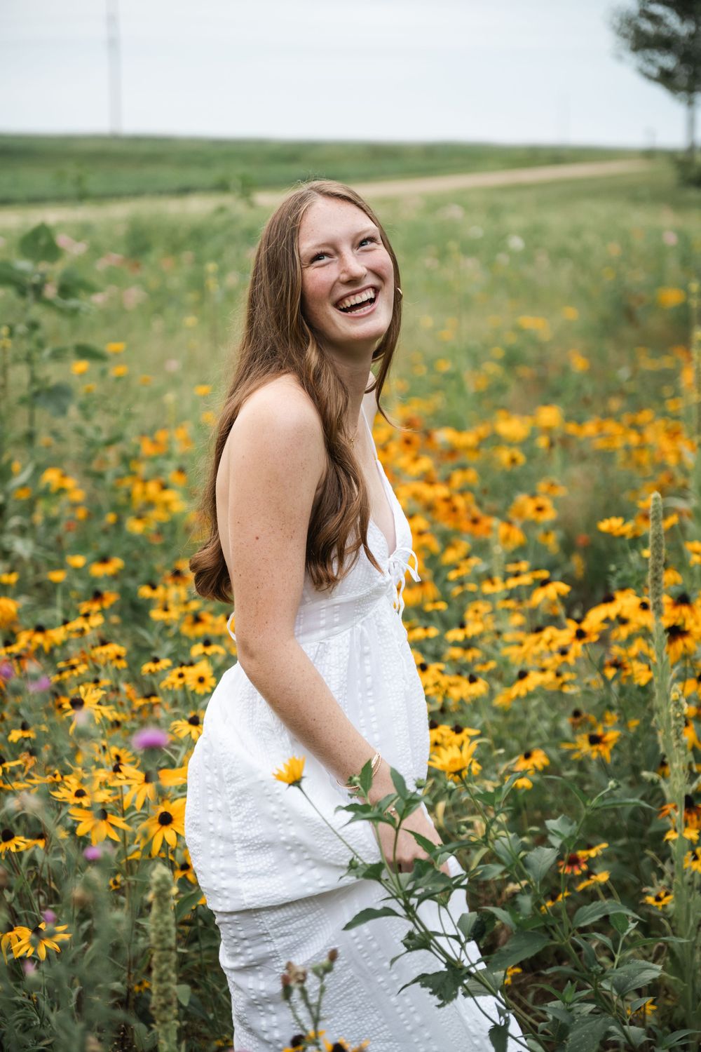 Woman in white dress laughing joyfully in field of yellow wildflowers.