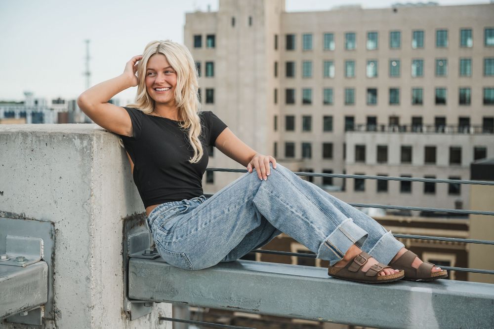 Casual rooftop portrait in black crop top and jeans with city buildings in background.