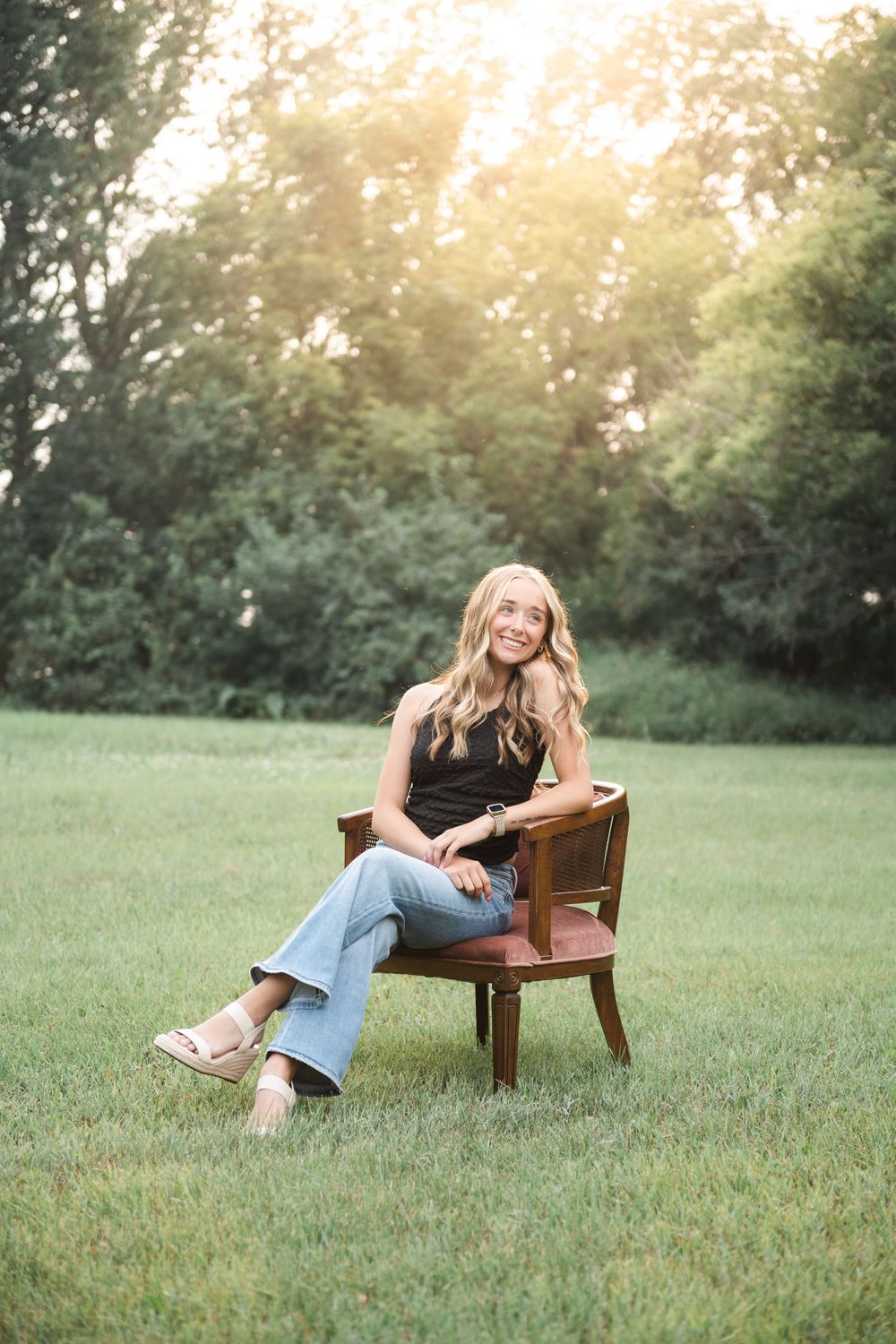 Woman relaxing on wooden chair in sunlit garden with golden hour lighting.