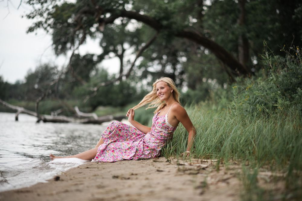 Woman in pink dress relaxing by waterfront during golden hour.