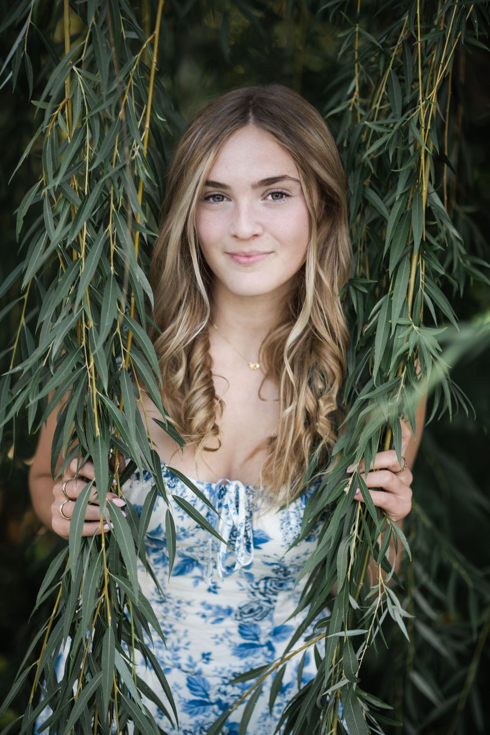 A sequence of outdoor portraits through hanging willow branches with blue and white floral dress creating a dreamy effect.