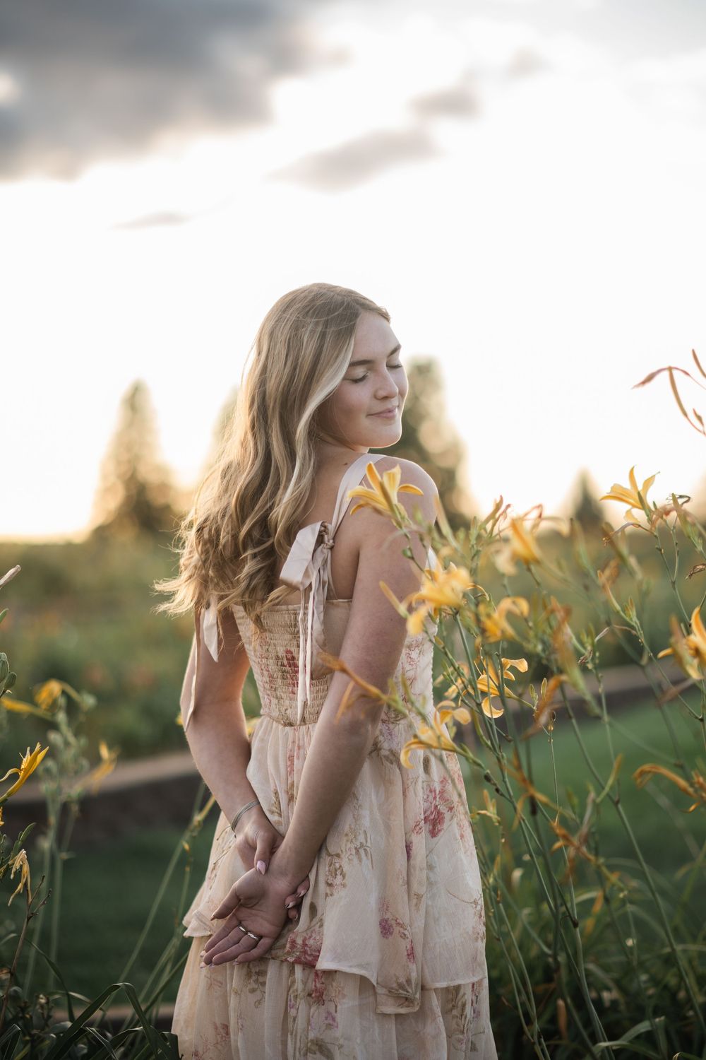 A person in a floral dress stands among yellow wildflowers in a field at sunset.