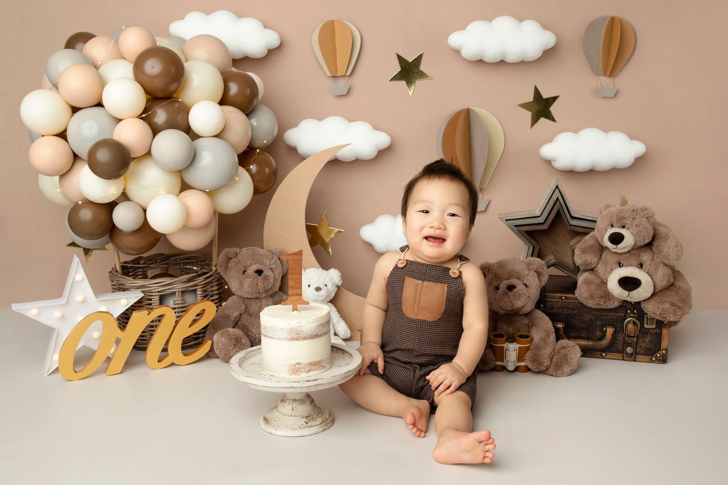 First birthday setup with neutral balloons, teddy bears, cake and hot air balloon decorations.