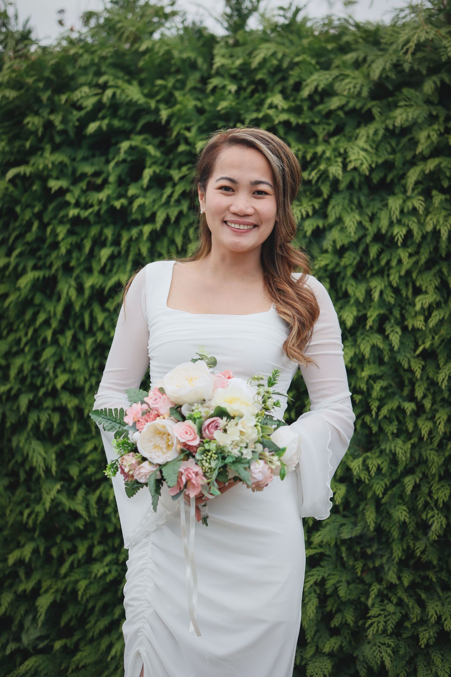 Bride in long-sleeved white dress holds elegant pink and white floral bouquet.