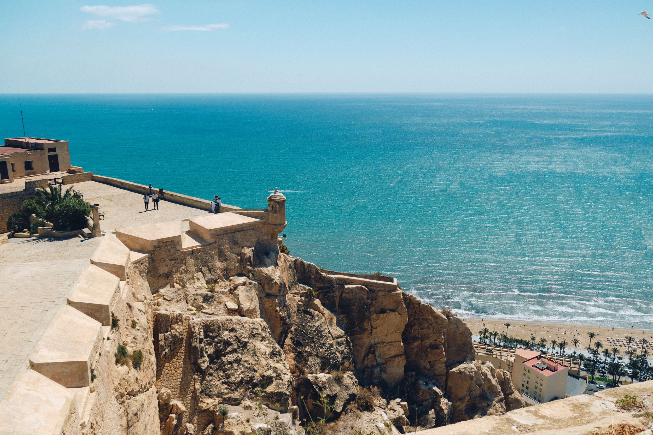 Stone fortress walls overlooking a beautiful turquoise beach and Mediterranean coastline.