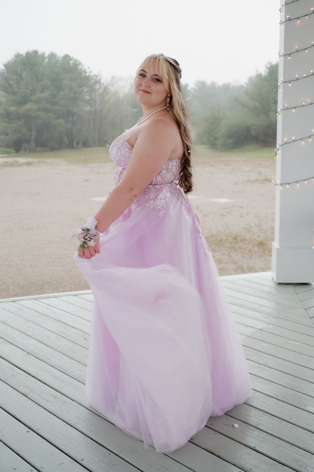 A person wearing a lavender ballgown with sparkly details poses on a wooden deck for a formal occasion.