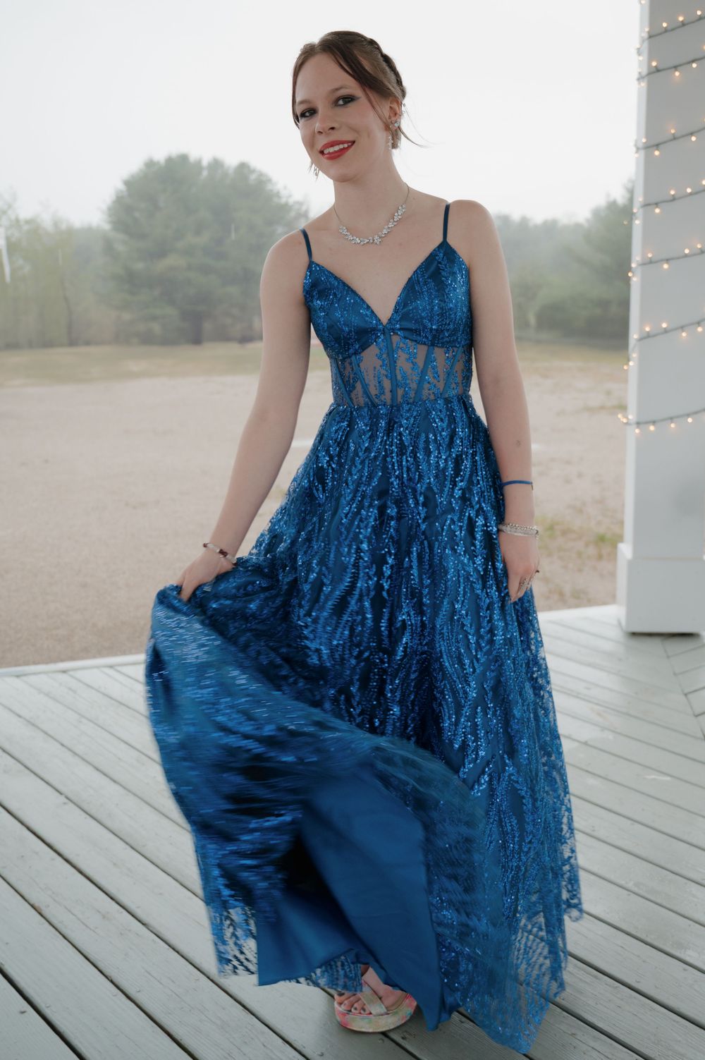 A person in a stunning royal blue sequined gown stands elegantly on a porch.