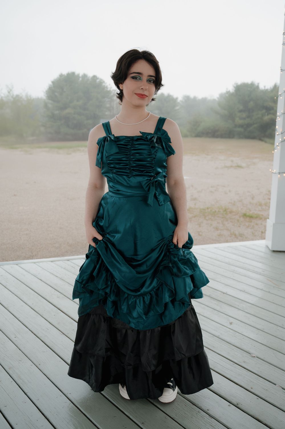 A person wearing an emerald green Victorian-style dress with ruffles poses on a wooden deck.