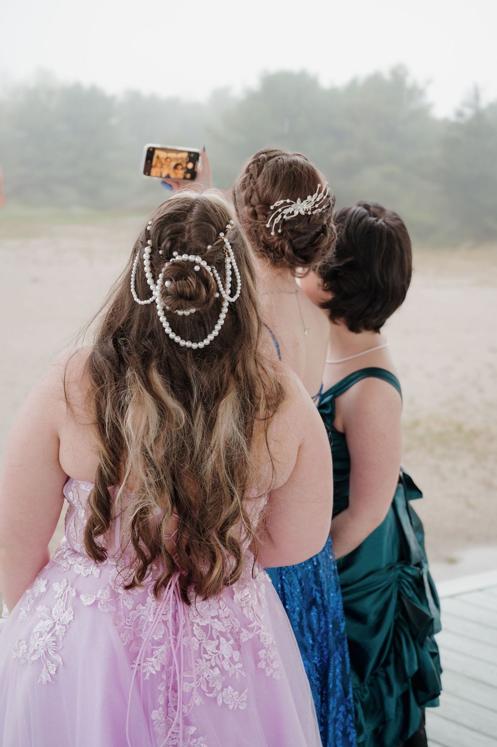 Friends taking selfies together on a deck while wearing formal dresses and hair accessories.