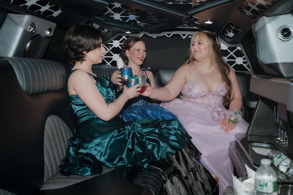 Friends enjoying drinks and conversation in a limousine while wearing formal gowns.