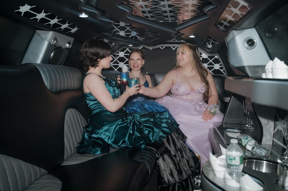 Friends in elegant dresses share drinks and laughter in the back of a decorated limousine.