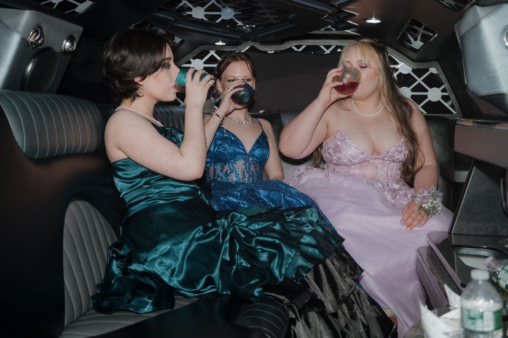 Three friends in formal attire enjoy refreshments while celebrating in a limousine.