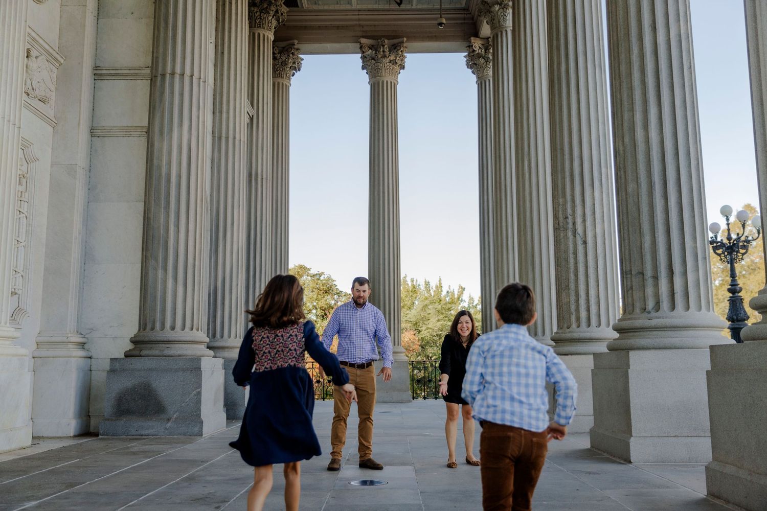 Visitors explore the grand columned entrance of a historic building with ornate classical architecture on a sunny day.