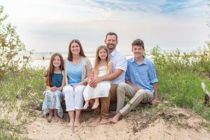 Family sitting together on a sandy beach dune during a summer photoshoot in coordinated blue and white outfits.