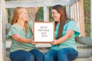 Two friends in turquoise shirts sit on a porch and share a laugh together during a sunny afternoon.