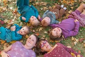 A group lying on autumn leaves wearing colorful sweaters and looking up at the sky together.