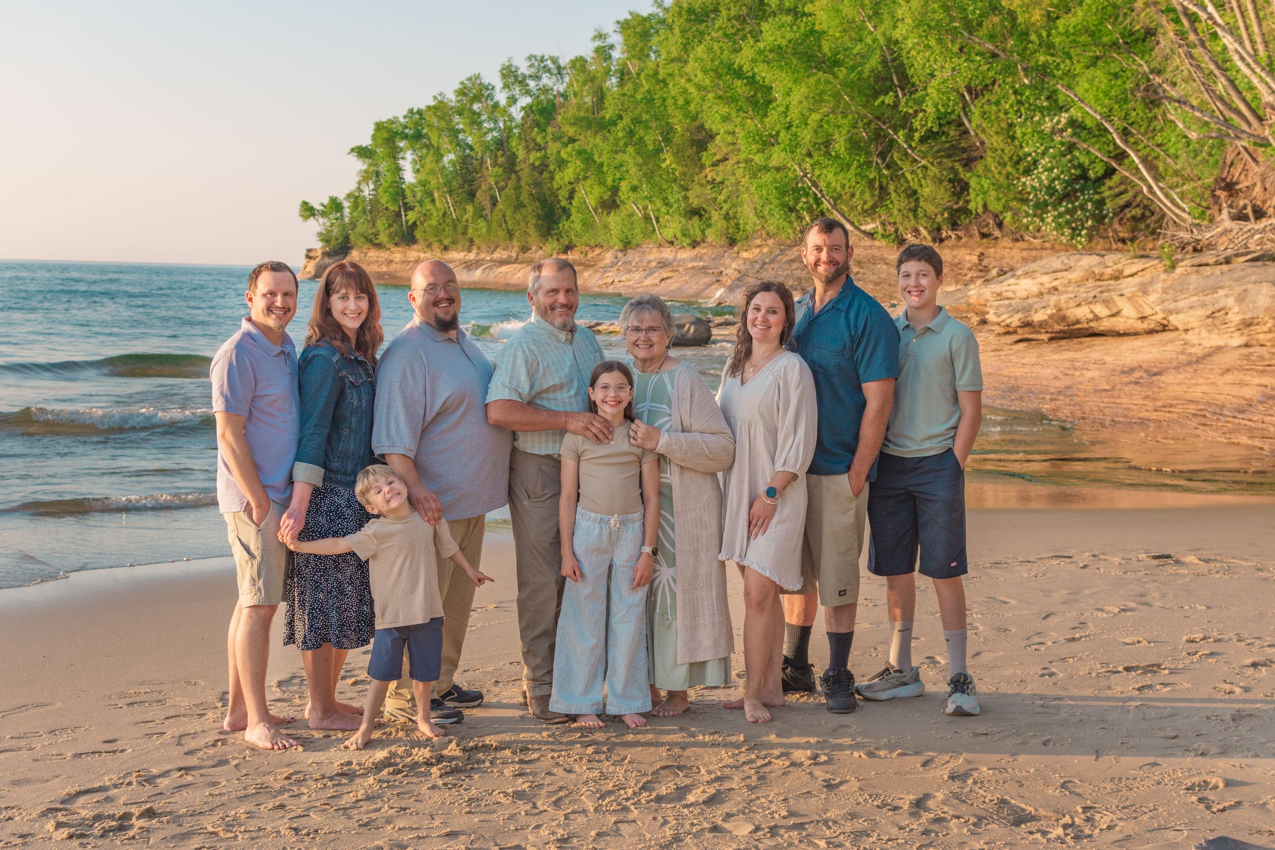 A group of people standing together on a sandy beach at sunset with ocean waves and cliffs in the background.