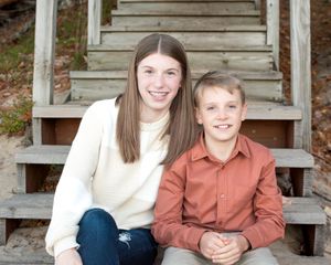 Family members sit together on wooden steps wearing coordinated rust orange and cream colored outfits for portraits.