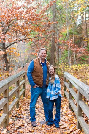 Two people stand on a wooden bridge surrounded by vibrant fall foliage and autumn leaves.