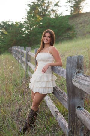 A white tiered sundress paired with brown cowboy boots creates a country chic look against a rustic wooden fence.