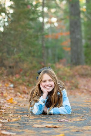 A young person lies on fallen autumn leaves wearing a blue and white striped sweater in a forest setting.