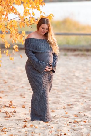 A person in a cozy gray sweater sits on autumn leaves beneath golden fall foliage at sunset.