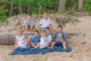 Group sitting together on a blue blanket at a sandy beach with trees in the background.