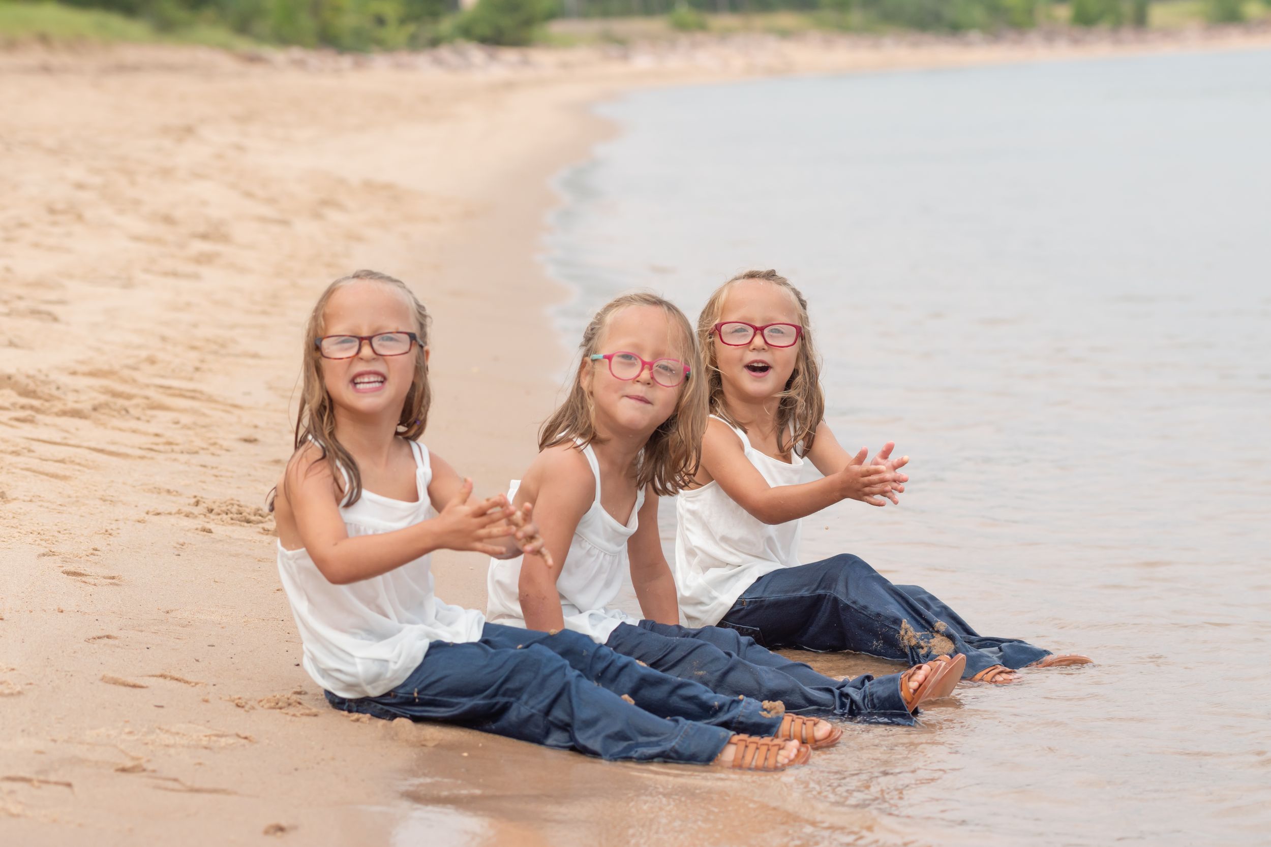 Three children in matching outfits sit together and laugh on a sandy beach.