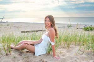 A white sundress on a sandy beach with dune grass and ocean waves in the background at sunset.