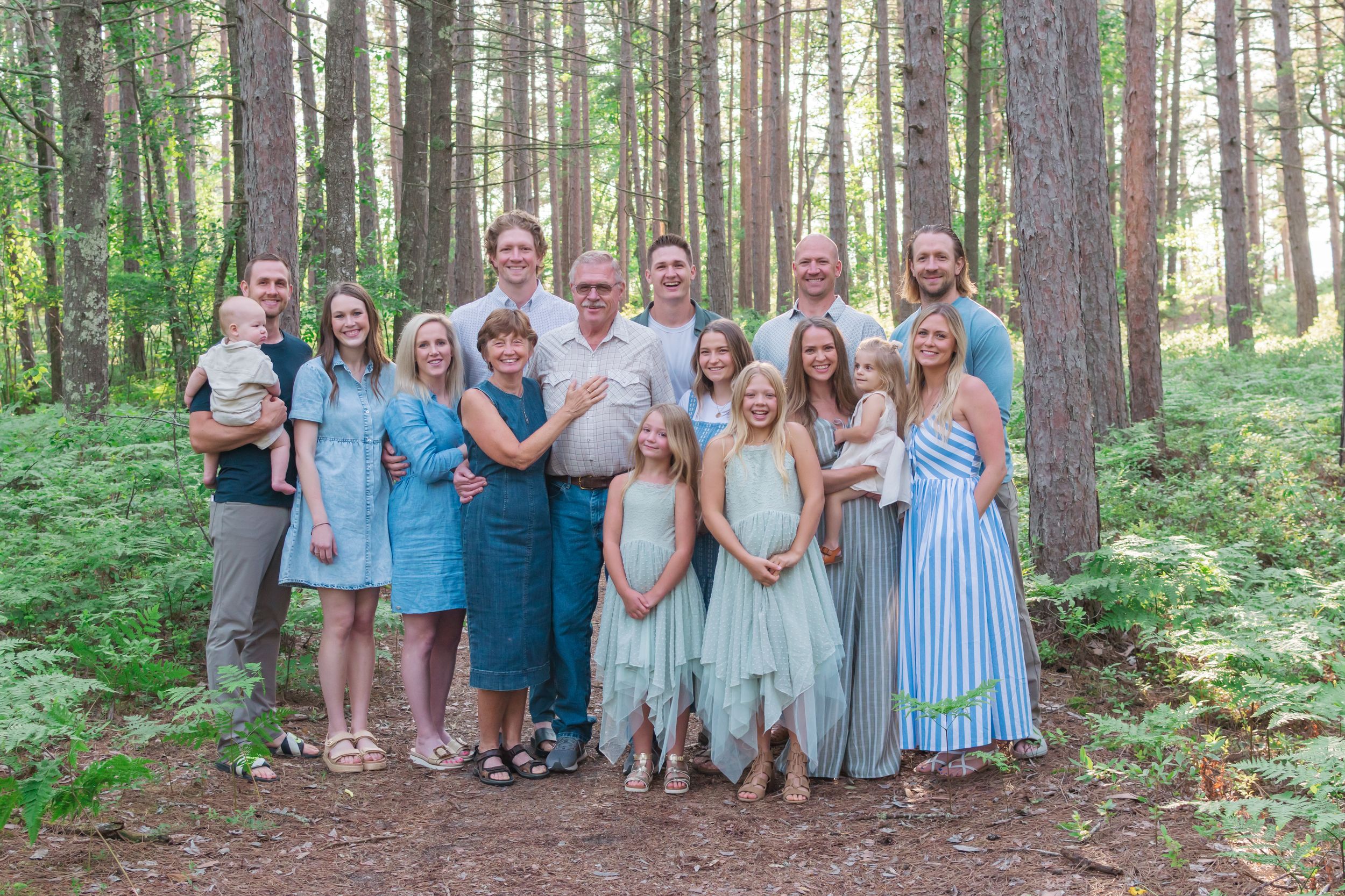 A group of people pose for a casual outdoor photo session in a wooded forest setting.