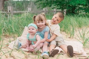 A family enjoys a sunny day together sitting in the sand dunes with tall grass and natural beach scenery.