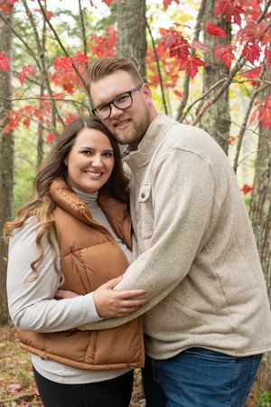 A couple shares tender moments in autumn woods with vibrant red maple leaves in the background.