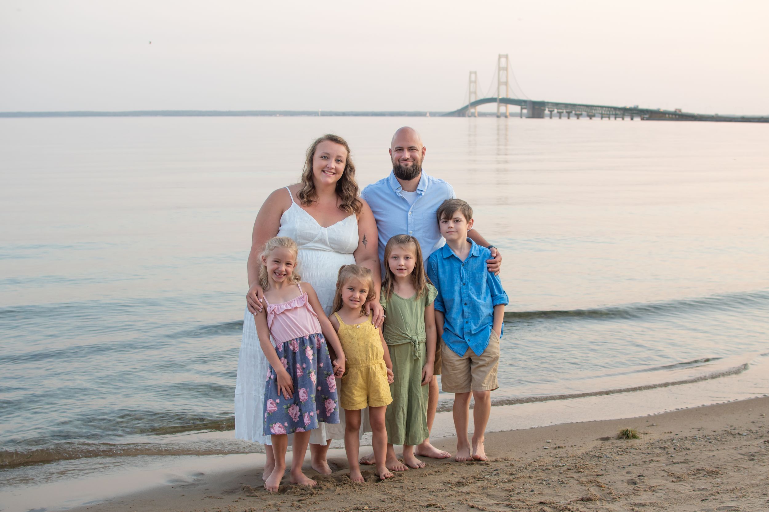 A family group poses together on a sandy beach at sunset wearing casual summer clothing.