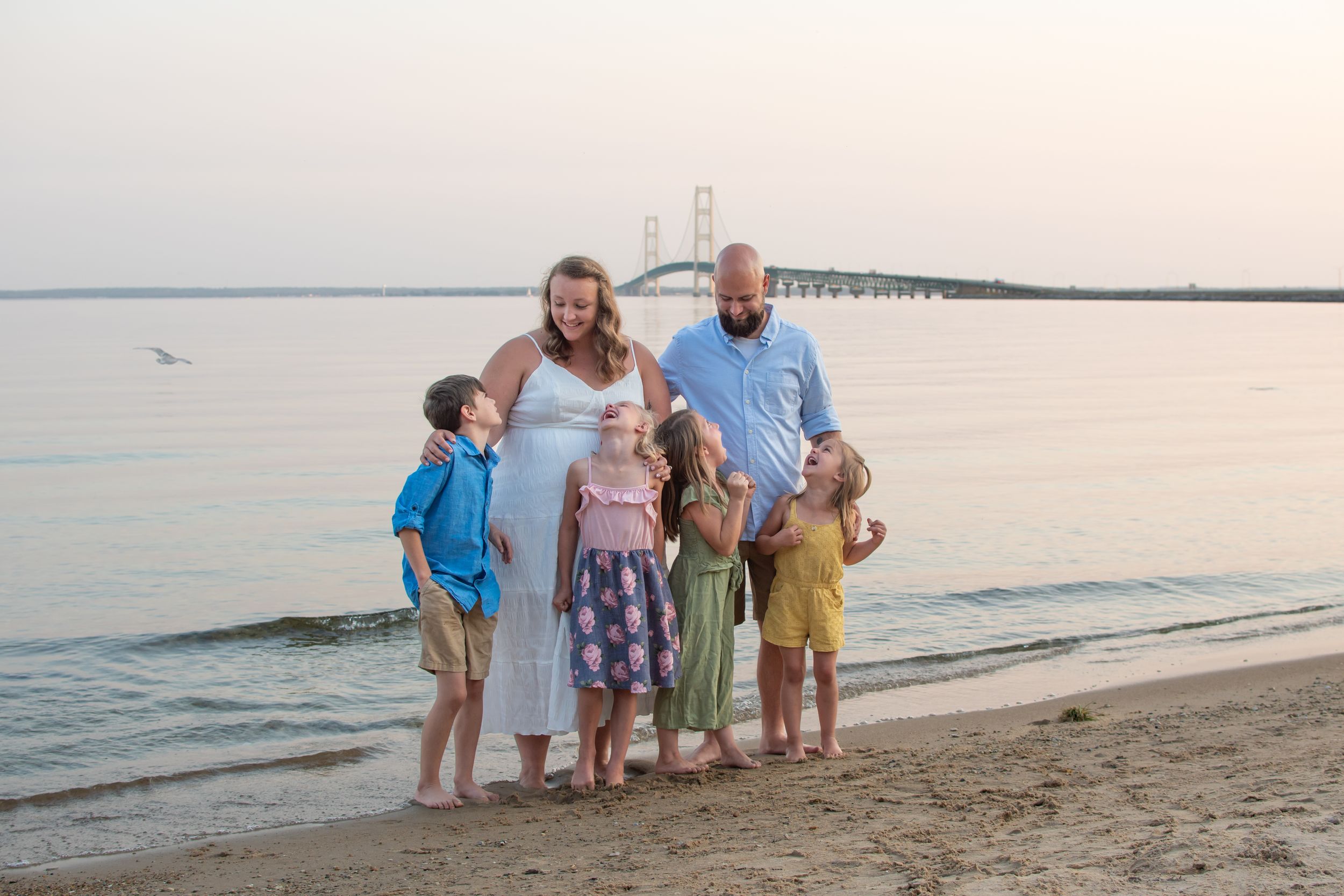 Family group standing together on a sandy beach at sunset with calm ocean waters in the background.