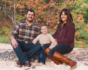 A family sits together on a rocky ledge surrounded by vibrant autumn foliage in the background.
