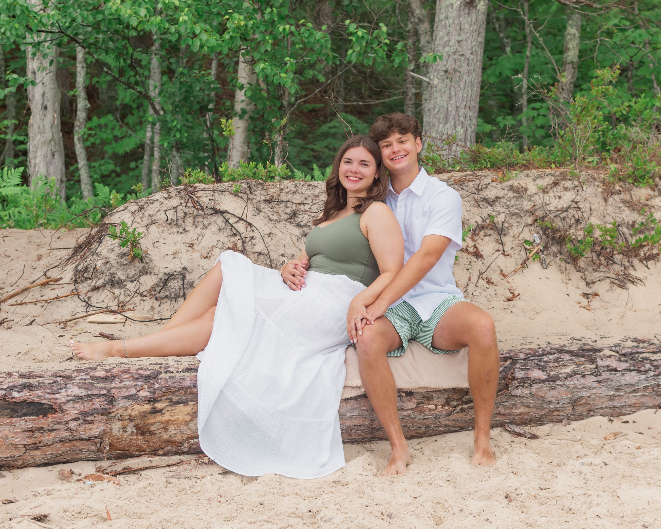 People in white outfits relaxing on a sandy beach with trees in the background.