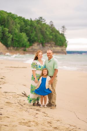 A family enjoying a peaceful moment together on a sandy beach with cliffs and trees in the background.