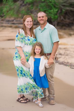 Family wearing coordinated blue and white outfits poses together on a sandy beach during a photo session.