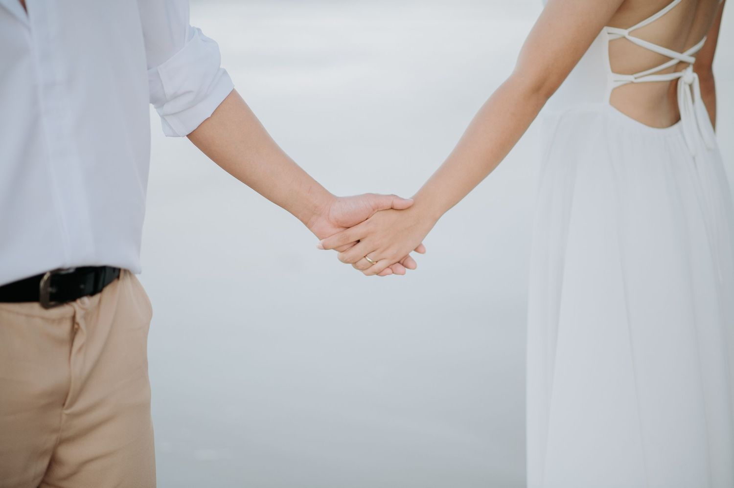 Close-up shot of a couple holding hands against a bright background.