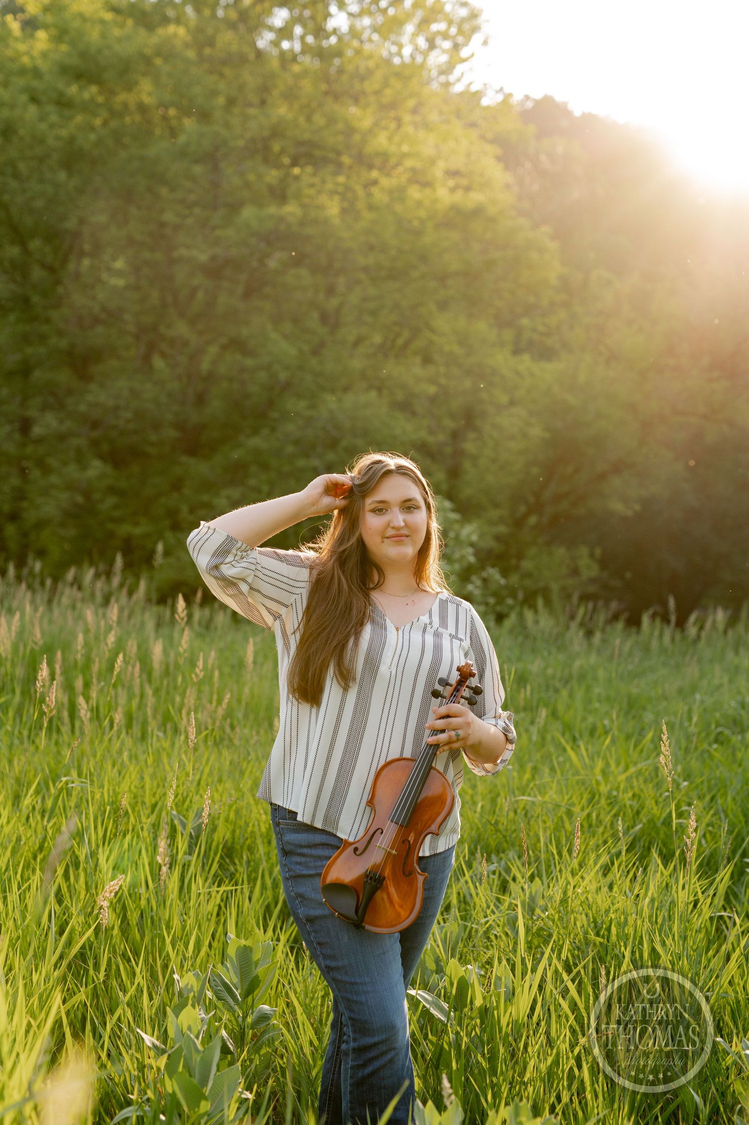 Musician stands with violin in sunlit meadow during golden hour.