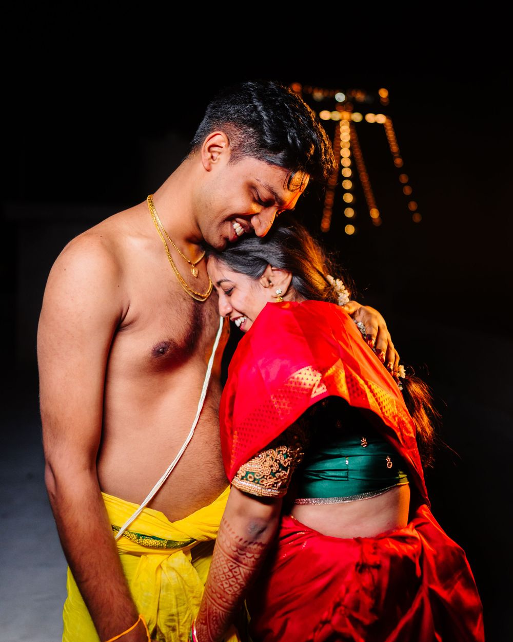 Romantic nighttime portrait against illuminated backdrop at Indian wedding celebration.