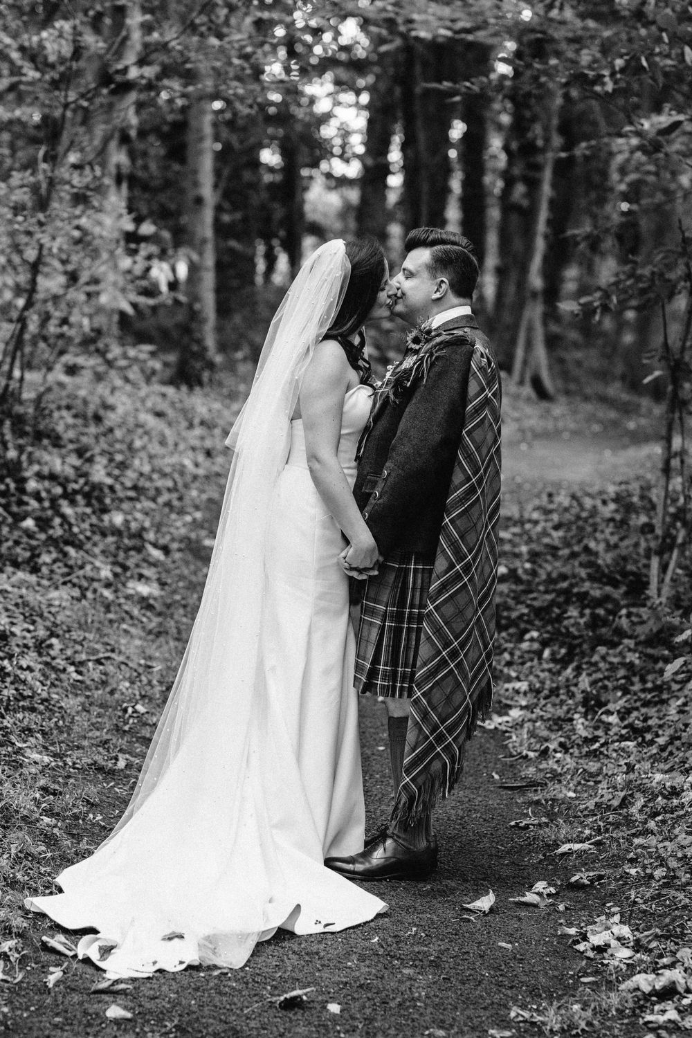 Black and white wedding photo of a couple sharing an intimate moment in the woods.