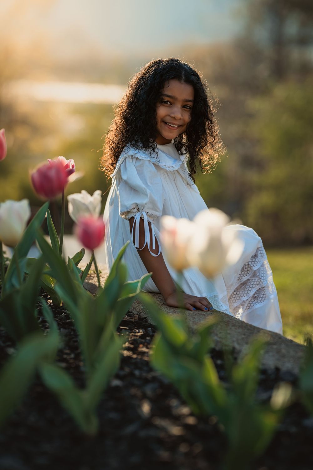 little girl with brown skin and hair sits beside some tulips in Spring