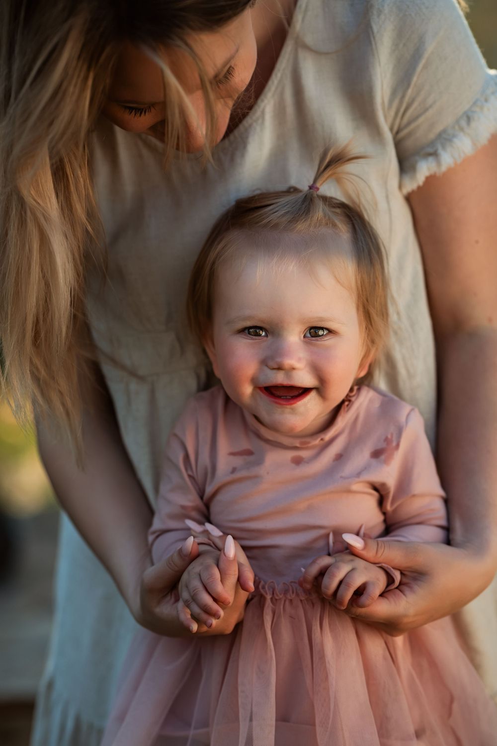 smiling baby girl holds onto her mom's hands for balance