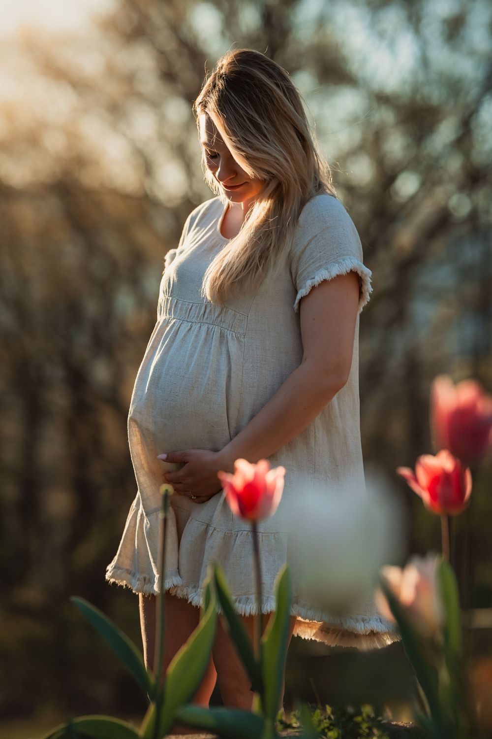 pregnant mama in short linen dress holds her belly among tulips
