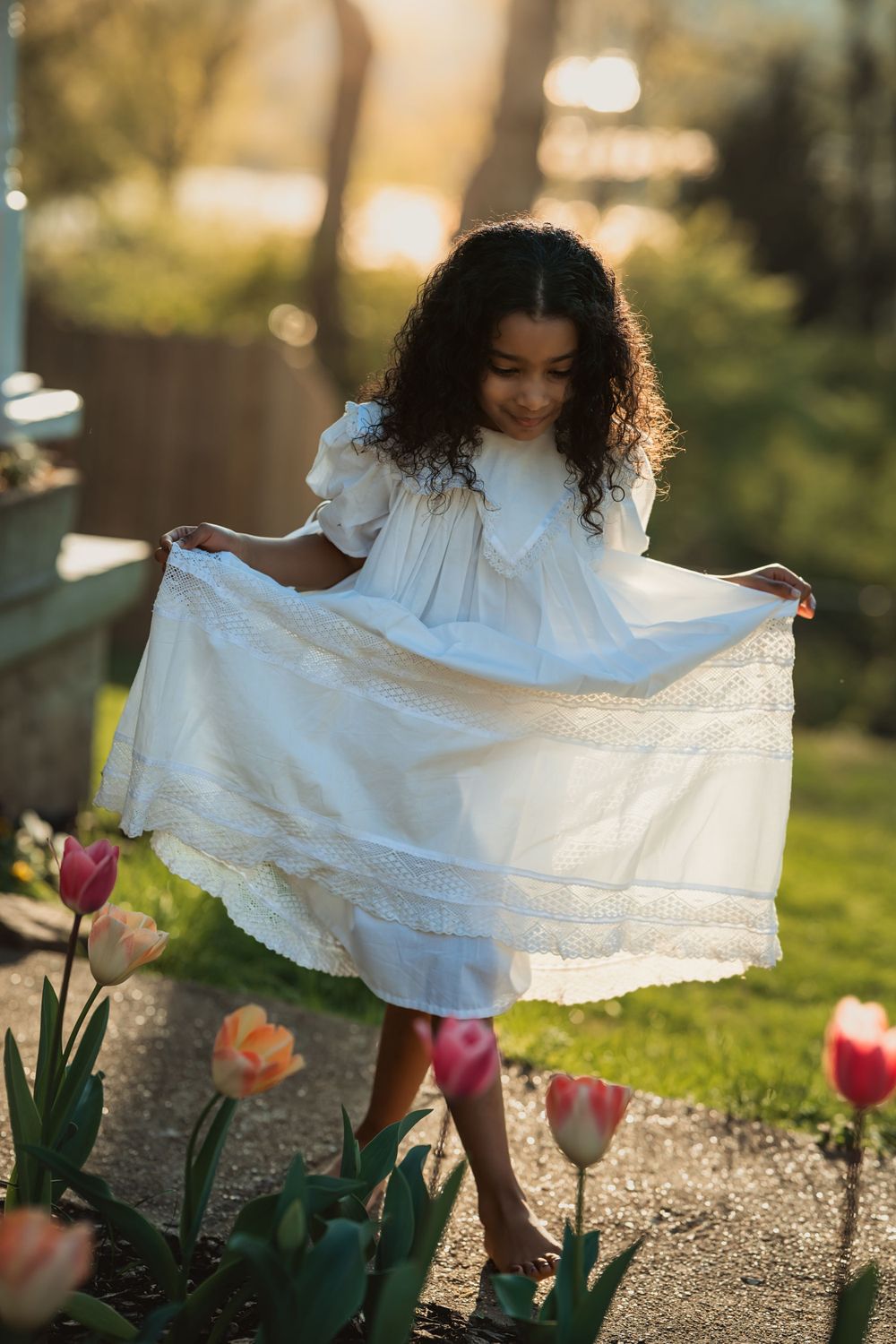 young girl in her mother's antique white dress holds it out as she walks past tulips
