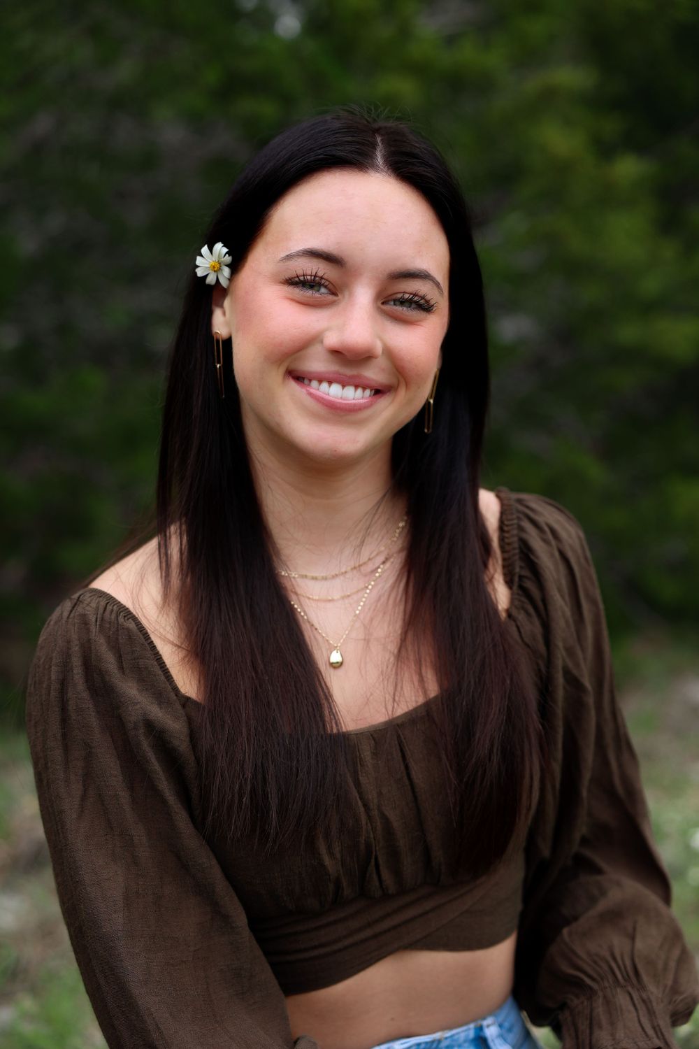 A candid outdoor portrait with a flower hair accessory against a natural background.