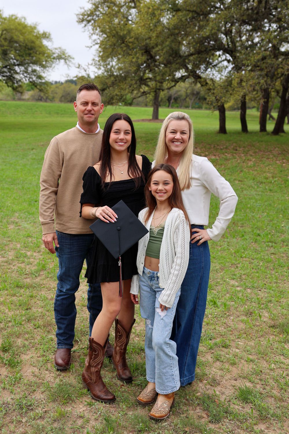 A group poses together outdoors for a graduation photo in a grassy field with trees.